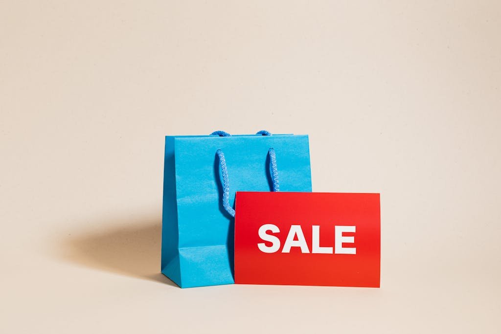 Blue shopping bag with red sale sign on neutral background, ideal for promotions.